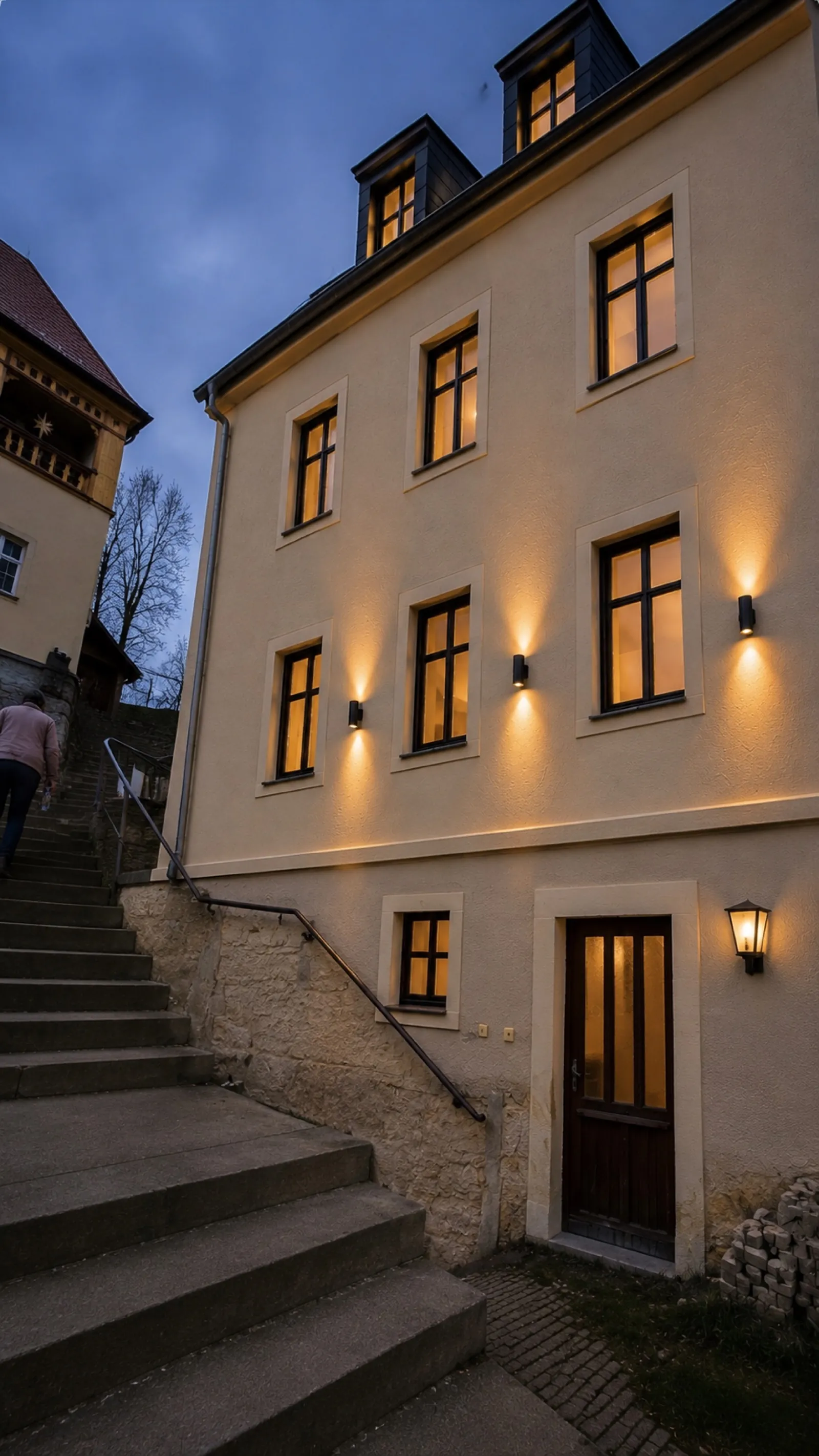 Beleuchteter Eingang des Apartmenthauses mit historischer Sandsteintreppe am Abend